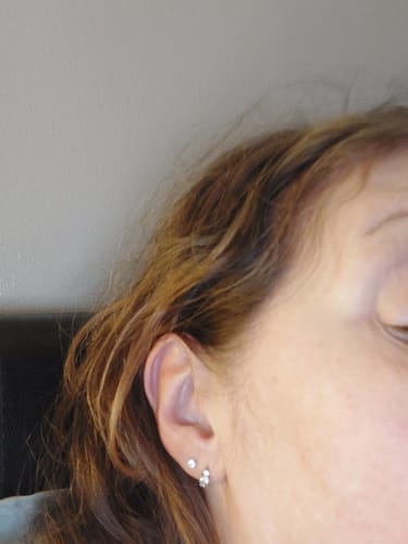 Customer's ear showing the delicate Midi Solitaire flatback Silver earring stacked with another sparkly earring.
