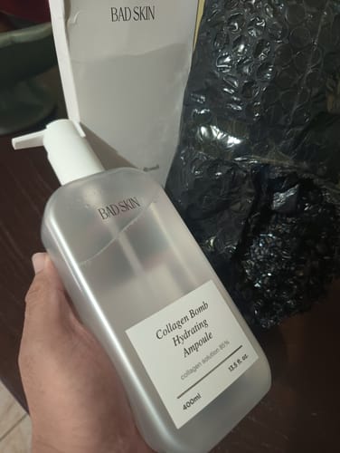 Customer holding the large, frosted bottle of Bad Skin Collagen Bomb Hydrating Ampoule.