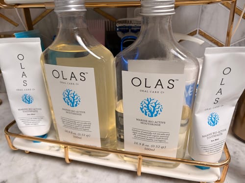 Reviewer's two tubes of OLAS Marine Sea Mint Toothpaste and matching mouthrinse bottles on a vanity tray.