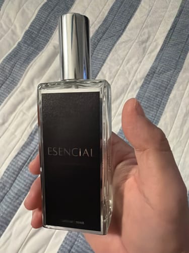 Reseñador sosteniendo en la mano el perfume rectangular Esencial H261 sobre un fondo de rayas.