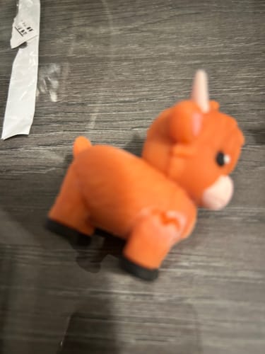 Close-up: Customer's damaged orange Highland Cow charm lying on a table.