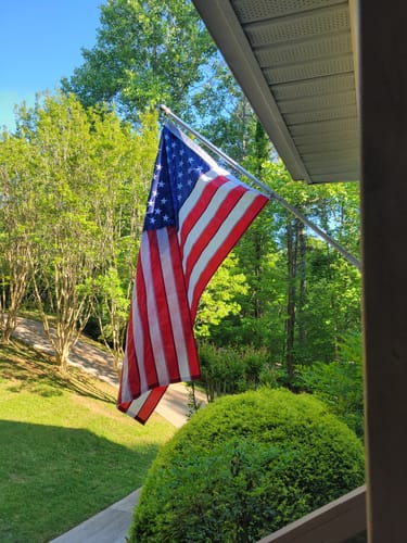 Customer's vibrant American Nylon Flag mounted on a pole outside a home, with green trees in the background.