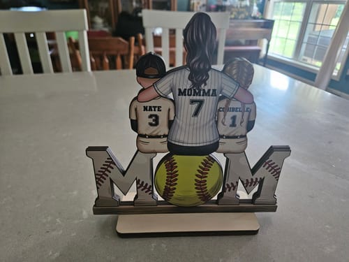 Reviewer's personalized wooden 'MOM' plaque. A mom and two kids in jerseys sit on top, with a softball used for the letter 'O'.