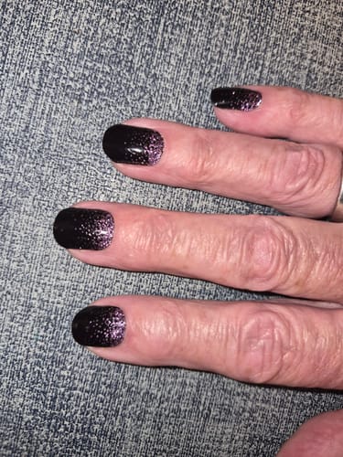 Hand eines Rezensenten mit den 'Twilight Romance' UV-Gel-Nagelfolien in schwarz mit lila Glitzer.