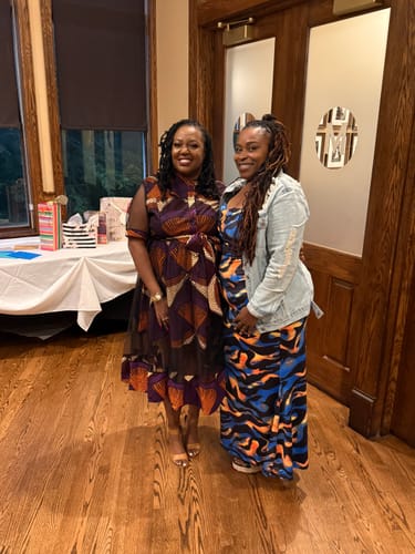 Reviewer standing with a friend while wearing the VALENTINA AFRICAN PRINT MESH DRESS with the matching sash tied at the waist.