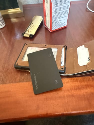 Reviewer's black SPOTMINDERS Tracking Card sitting on top of an open wallet on a wooden desk.
