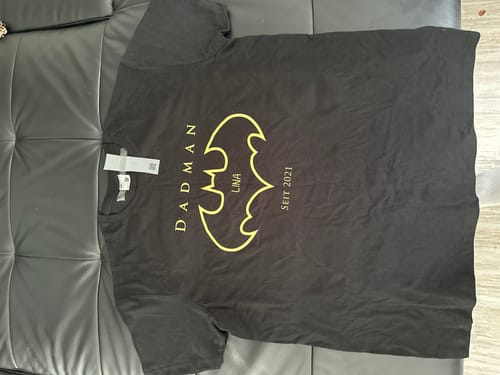 Ein Kunde zeigt das personalisierte schwarze „Der Dadman“-T-Shirt, das auf einer Ledercouch liegt.