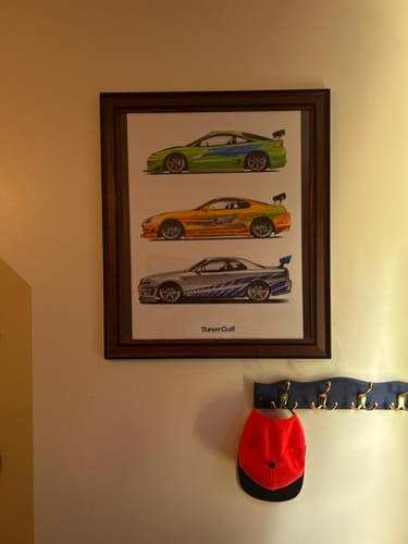 Customer's framed 'Fast Rides' poster showing three illustrated cars, hanging on a wall.