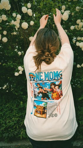 Kundin zeigt die Rückseite ihres ONE MOM T-Shirts mit großem, buntem Aufdruck im Freien.
