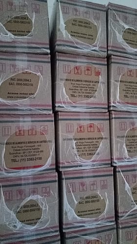Cliente mostra as caixas de papelão da Cesta Básica Araucária empilhadas umas sobre as outras.