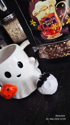 Kunde zeigt die Packung Butterscotch Brew Tee neben einer Geistertasse und Halloween-Dekoration.