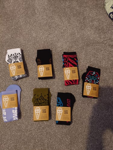 Customer's seven pairs of colorful Compression Shred Socks from the lucky dip pack laid out on a carpet, still in their packaging.