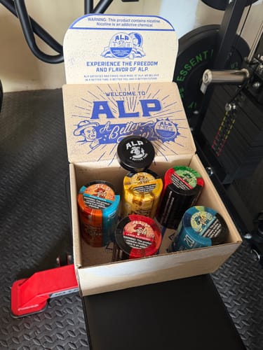 Customer's black Metal Travel Tin sitting atop several colorful tins inside an open ALP delivery box.