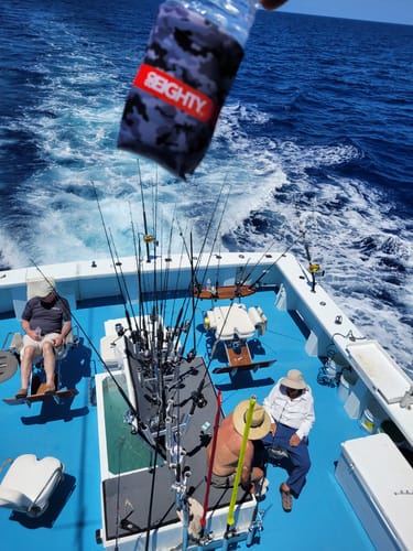 Reviewer holding an 80Eighty® Camo Koozie on a water bottle above a fishing boat deck.
