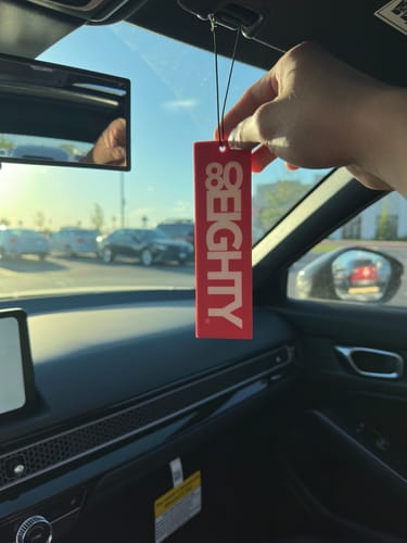 Customer holding the red 80Eighty Smoke Ice Air Freshener while hanging it inside a car.