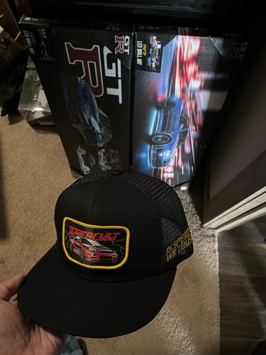 Customer holding a black SKYLINE TRUCKER HAT, showing its embroidered patch with a red car design.