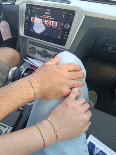 Close-up of two people's wrists wearing matching silver knot bracelets while in a car.
