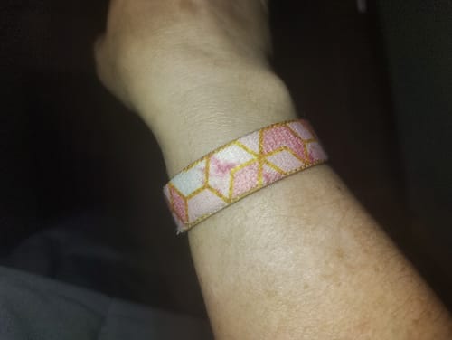 Close-up of a customer's wrist, wearing the She Believed She Could Bracelet with its pink and gold geometric design.