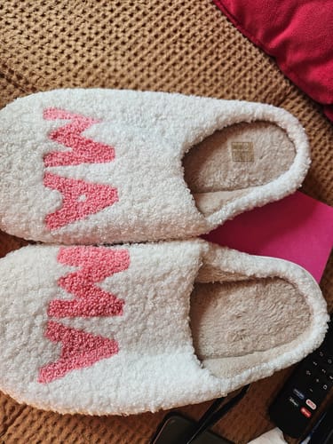 Customer's pair of white plush Mom Essential Slippers with 'MAMA' in pink text on a textured surface.