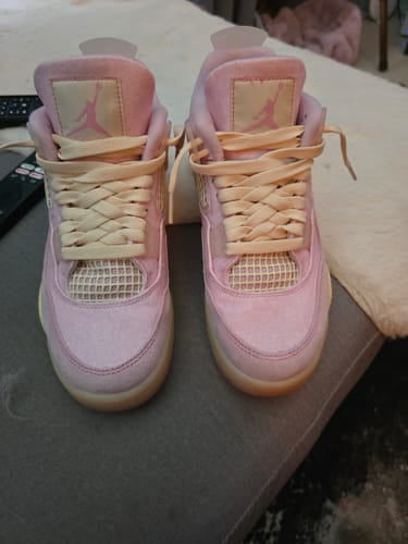 Recensent toont een paar roze Jordan 4 Retro Iced Carmine sneakers met crèmekleurige veters.