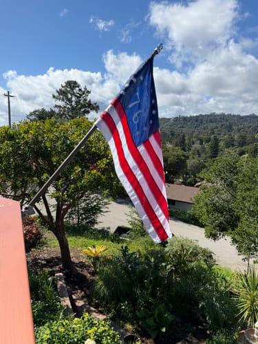 Customer's Bennington '76' flag flying from a bronze-colored flagpole against a partly cloudy sky.
