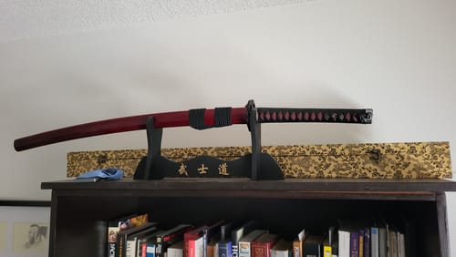 Customer's custom Japanese sword with a red gradient sheath and black handle, displayed on a stand.
