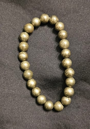 Customer's beaded pyrite bracelet lying in an oval on a dark textured surface.