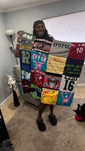 Reviewer smiling while holding up their colorful Project Repat T-Shirt Quilt made from various t-shirts.