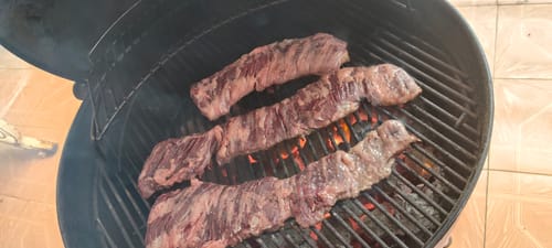 Reseñador asando tiras de Arrachera Outside Limpia en una parrilla de carbón.