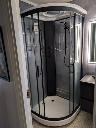 Anmelderens bad med Amsterdam Grå selvklebende fliser på veggene rundt en moderne, avrundet dusj med svarte detaljer.