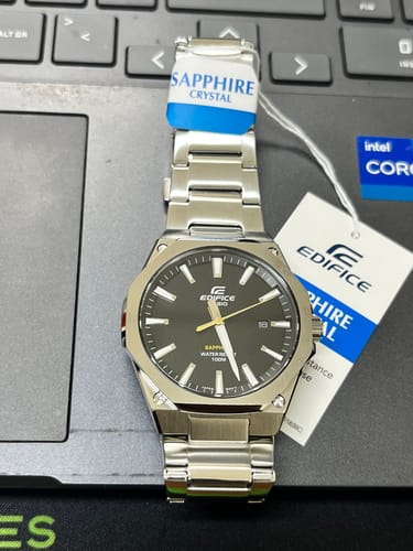 Reloj Casio Edifice metálico de un cliente, con esfera negra, sobre el teclado de un portátil con las etiquetas puestas.