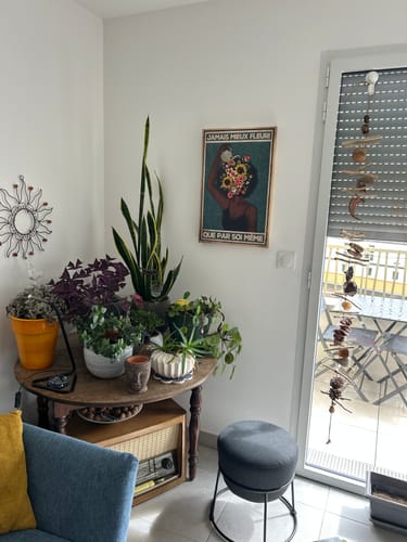 La toile Jamais mieux fleuri que par soi-même installée dans le salon de Sylvie, entourée de plantes vertes.