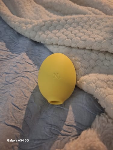 Reviewer's yellow Lem Clitoral Massager resting on a textured bedspread.