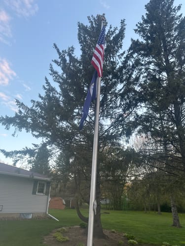 Customer's United States Navy Flag flying on a flagpole below an American flag in a yard with large trees.
