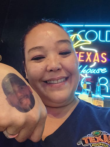 Reviewer smiling while showing a custom temporary tattoo of a person's face on the back of their hand.