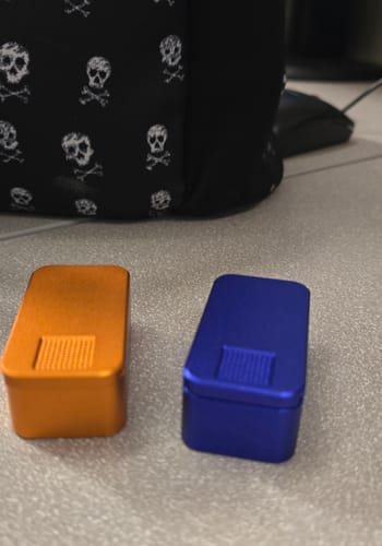 Customer's orange and blue metal pill cases from the 2-pack bundle on a desk.