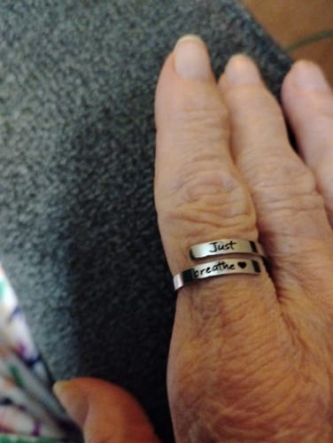 Close-up of a reviewer's thumb wearing a silver wrap ring engraved with 'Just breathe' and a heart.