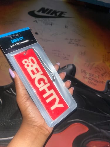 A reviewer holds up a red 80Eighty air freshener, still in its original packaging.