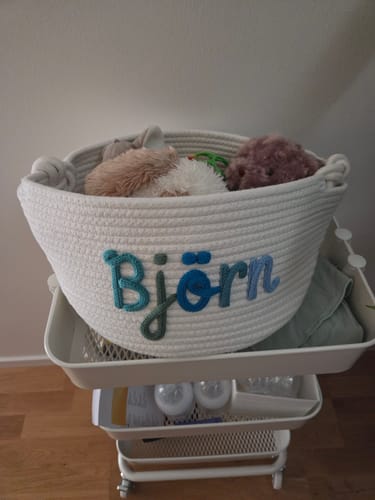 Customer's personalized white woven basket with the name 'Björn', filled with soft toys on a utility cart.