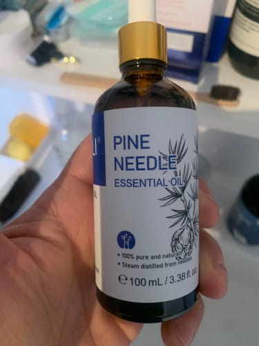 Customer holding the 100 mL brown glass bottle of Pine Needle Essential Oil, showing the product label.