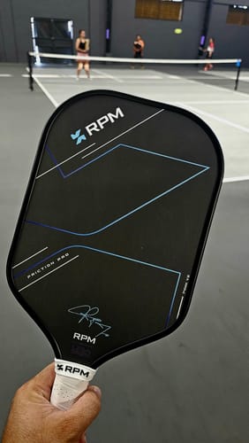 Customer holding the black RPM Friction Pro Elongated V2 paddle on a pickleball court.