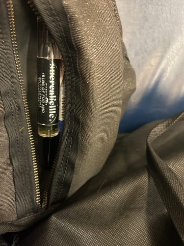 Reviewer's '15lbs Of Fur and Entitlement' 10ml perfume spray bottle shown peeking out of a zippered bag pocket.
