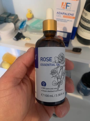 Customer holding a brown bottle of Rose Essential Oil with a white label and dropper.