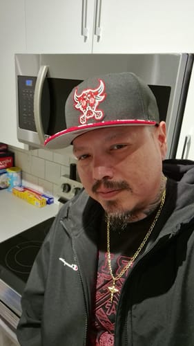 Reviewer wearing the gold-colored Sacred Crucifix Necklace over a black shirt in a kitchen setting.