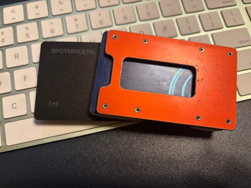 Customer's black SPOTMINDERS Tracking Card shown next to an orange minimalist wallet on a keyboard.