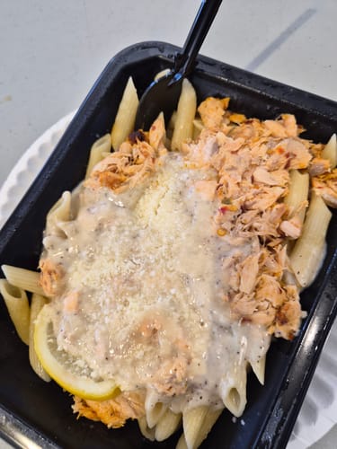 Customer's Salmon Alfredo meal in a black container, with creamy alfredo sauce, shredded salmon, and a lemon slice.