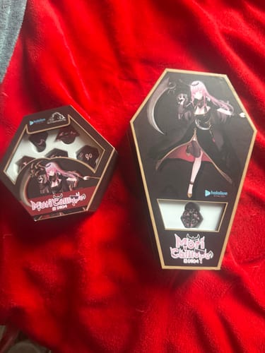 Customer's two Mori Calliope dice set boxes from the collection bundle, one hexagonal and one coffin-shaped, on a red blanket.