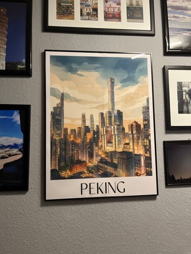 Ein Kunde zeigt das Peking-Poster in einem schwarzen Rahmen, das an einer grauen Wand zwischen anderen Bildern hängt.