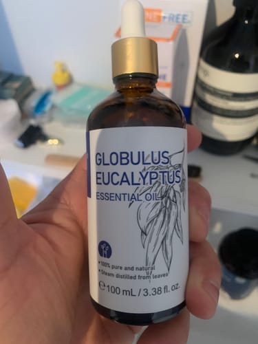 A customer's hand holds a brown glass dropper bottle of Globulus Eucalyptus Essential Oil.