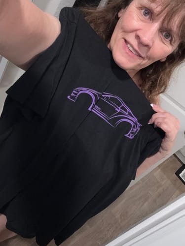 A smiling reviewer holds up the black 80Eighty® DCG88 Shirt to show off the purple car graphic.